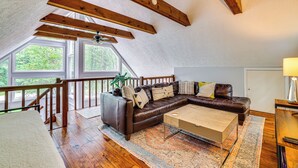 A cozy loft bedroom with a sloped ceiling, wooden beams, a large window, a brown leather sofa, a wooden coffee table, and a desk with a lamp. - 15 Mi to Ski Resort: Home w/ Fire Pit in Tobyhanna (Tobyhanna)