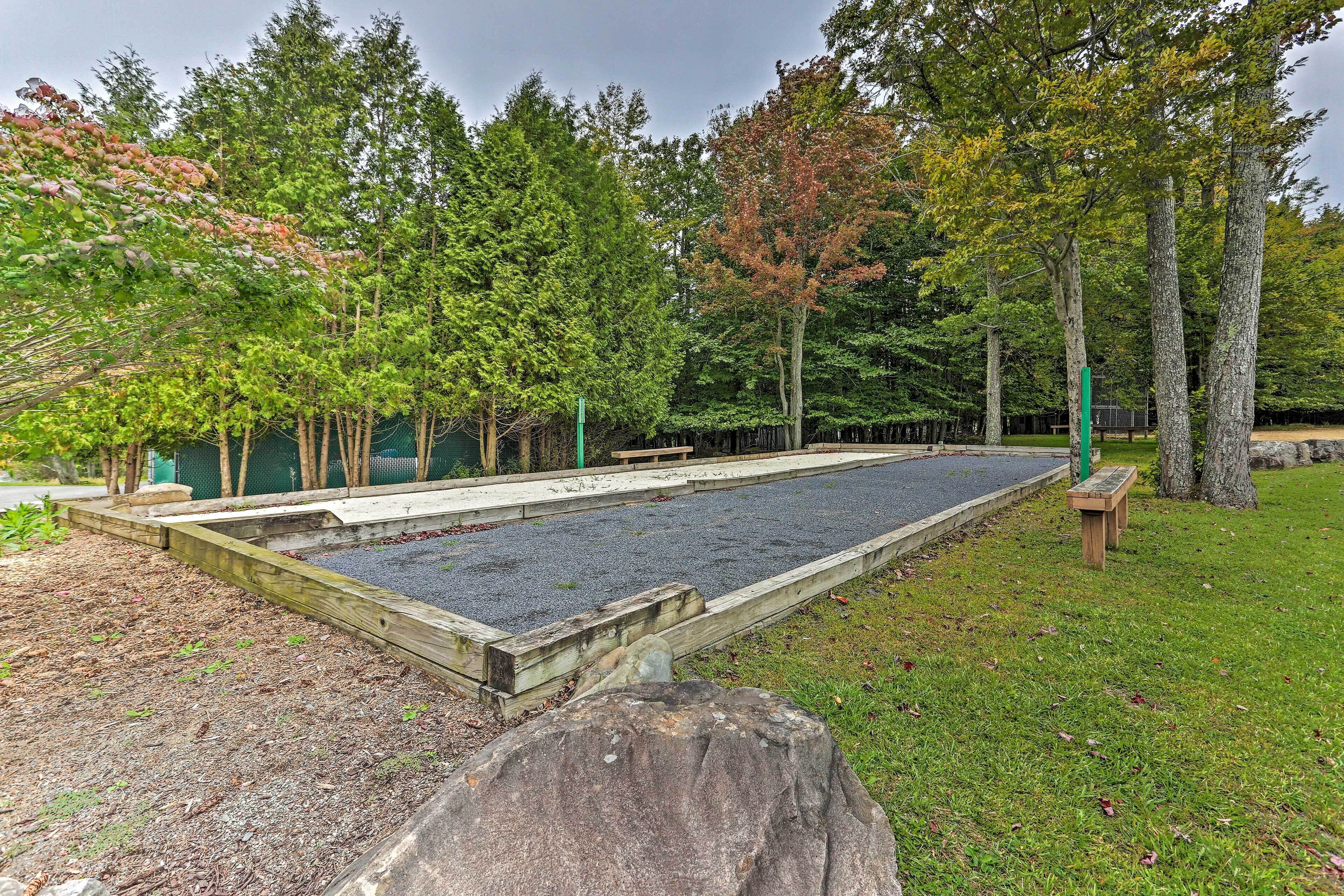 Una terraza de madera con un sendero de piedra, rodeada de árboles y un área verde.
