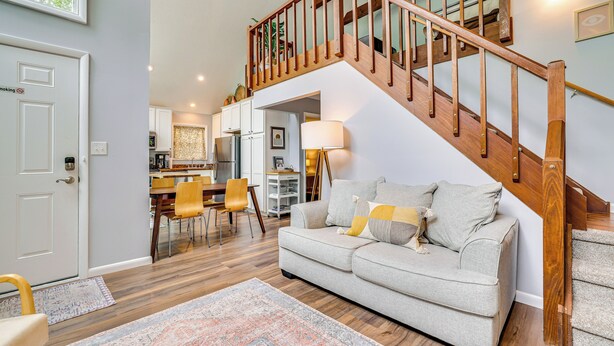 A living room with a wooden staircase, a sofa, a dining area, and a kitchen in the background. - 15 Mi to Ski Resort: Home w/ Fire Pit in Tobyhanna (Tobyhanna)