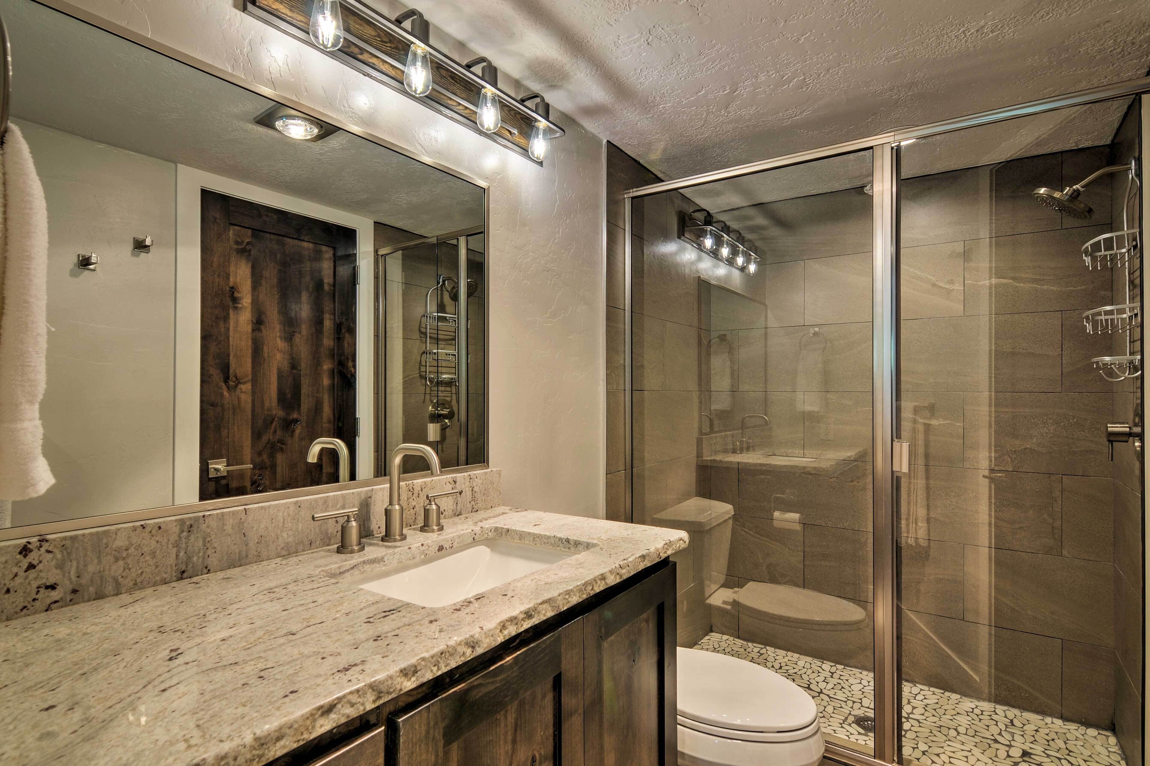 A bathroom with a marble countertop, a sink, a mirror, a shower with a glass door, and a toilet.