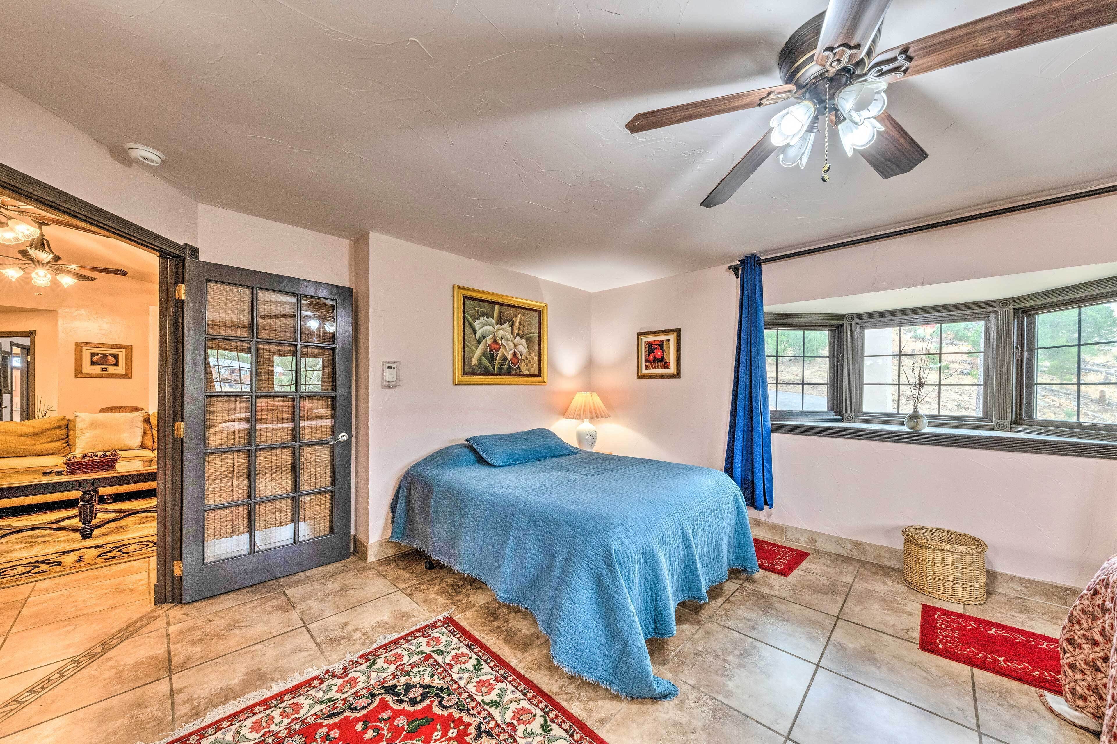 A bedroom with a bed, a ceiling fan, a window, and a door leading to another room.