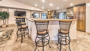 A modern kitchen with a central island, bar stools, wooden cabinets, and a large window. - Hot Tub & Mtn Views! 'casa Ruidoso' Cabin (Alto)