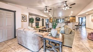 A spacious living room with a beige sofa, a coffee table, and a fireplace. There are ceiling fans and a TV mounted on the wall. - Hot Tub & Mtn Views! 'casa Ruidoso' Cabin (Alto)