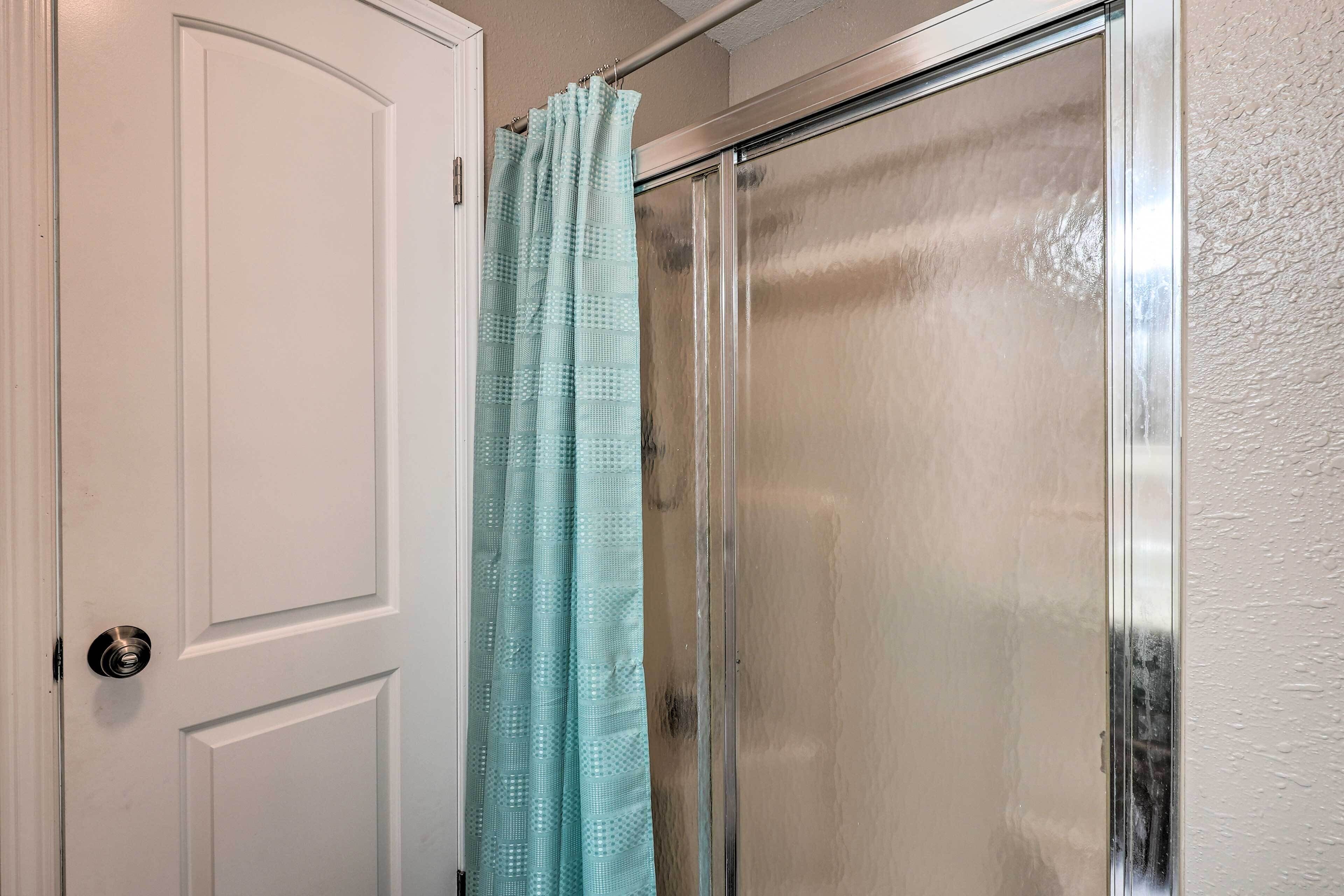 A bathroom with a white door, a shower with a glass door, and a light blue shower curtain.
