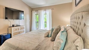 A bedroom with a large bed, a flat-screen TV mounted on the wall, a dresser, and a window with curtains. - Reeds Spring Condo Near Aquarium at the Boardwalk! (Branson West)