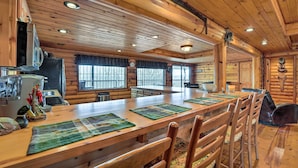 A spacious wooden cabin with a long dining table, chairs, and a kitchen area. - Rustic Cabin in Roaring River State Park! (Eagle Rock)