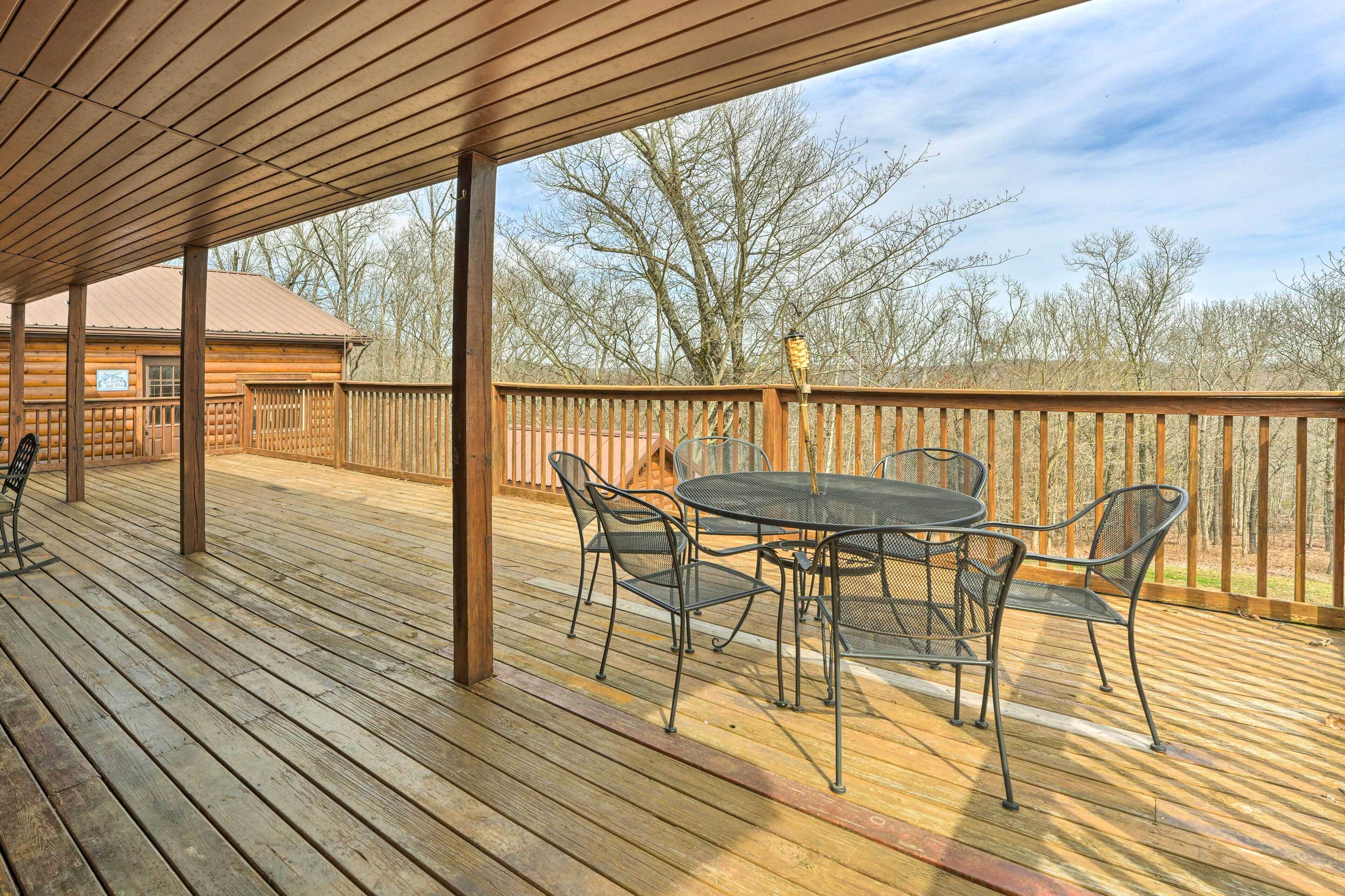 A wooden deck with a table and chairs, a wooden fence, and a view of trees and a building in the background.