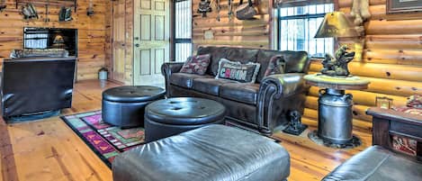 L’intérieur d’une cabane en rondins, avec un canapé en cuir, des poufs, une cheminée et un décor rustique.