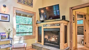 Ein gemütliches Wohnzimmer mit Kamin, einem darüber montierten Fernseher und einem Bücherregal mit Büchern und Dekoration.