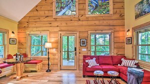 Ein gemütliches Blockhaus-Interieur mit Holzwänden, einem roten Sofa, einem Holztisch und großen Fenstern.