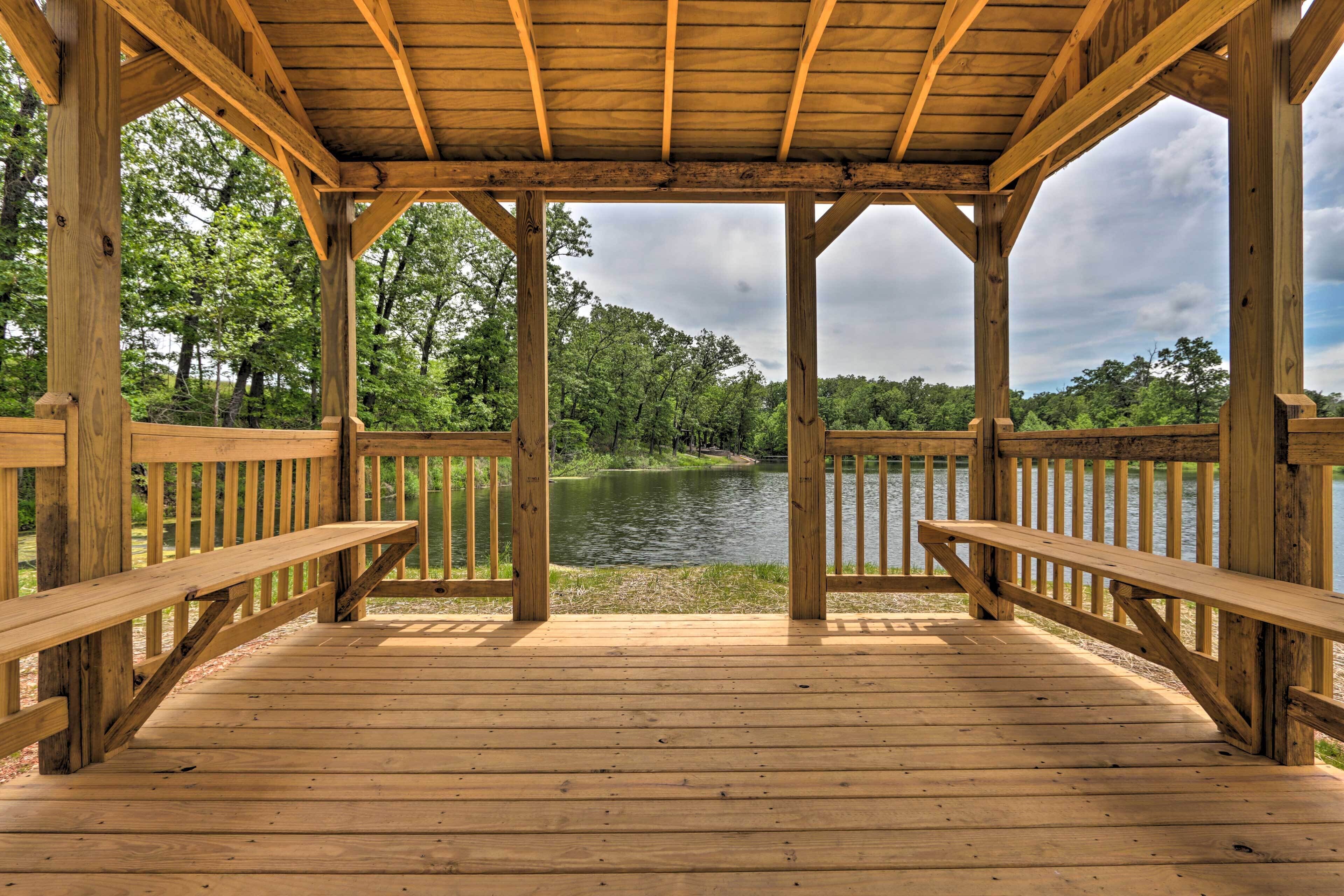 Une terrasse en bois avec des bancs, donnant sur un lac et entourée d’arbres.