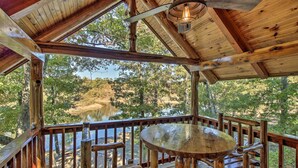 A wooden deck with a round table and benches, overlooking a natural landscape with trees and a body of water.