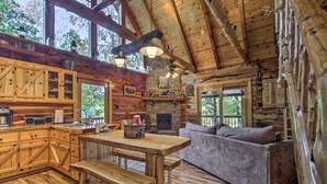 A rustic cabin interior with a wooden dining table, bench, sofa, and a fireplace.