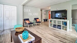 En moderne stue med tv, siddeområde og en væg med teksten 'OAK ISLAND'.