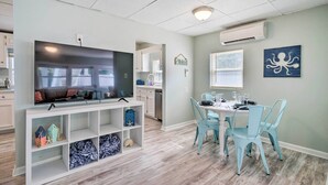 En moderne stue med et fladskærms-tv, et spiseområde med blå stole og et køkken i baggrunden.