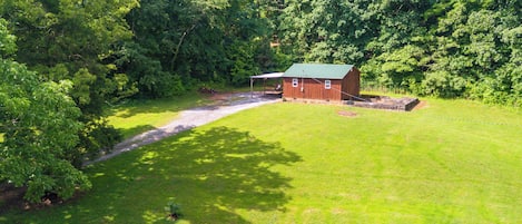 A red barn with a green roof, surrounded by a lush green field and dense trees.