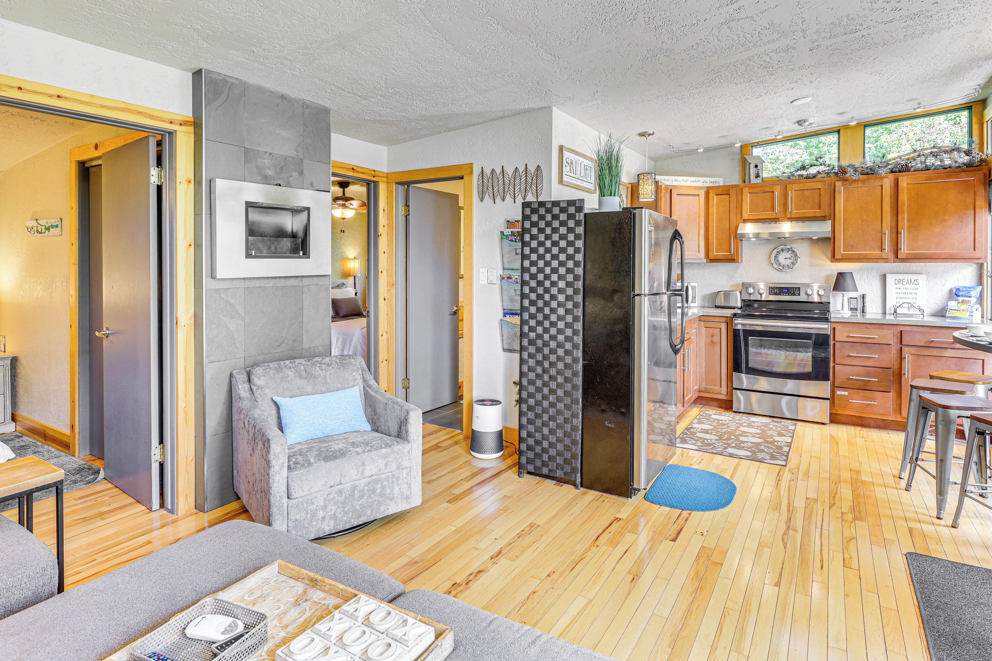 A compact living space with a kitchenette, a grey sofa, a small dining area, and a wooden floor.
