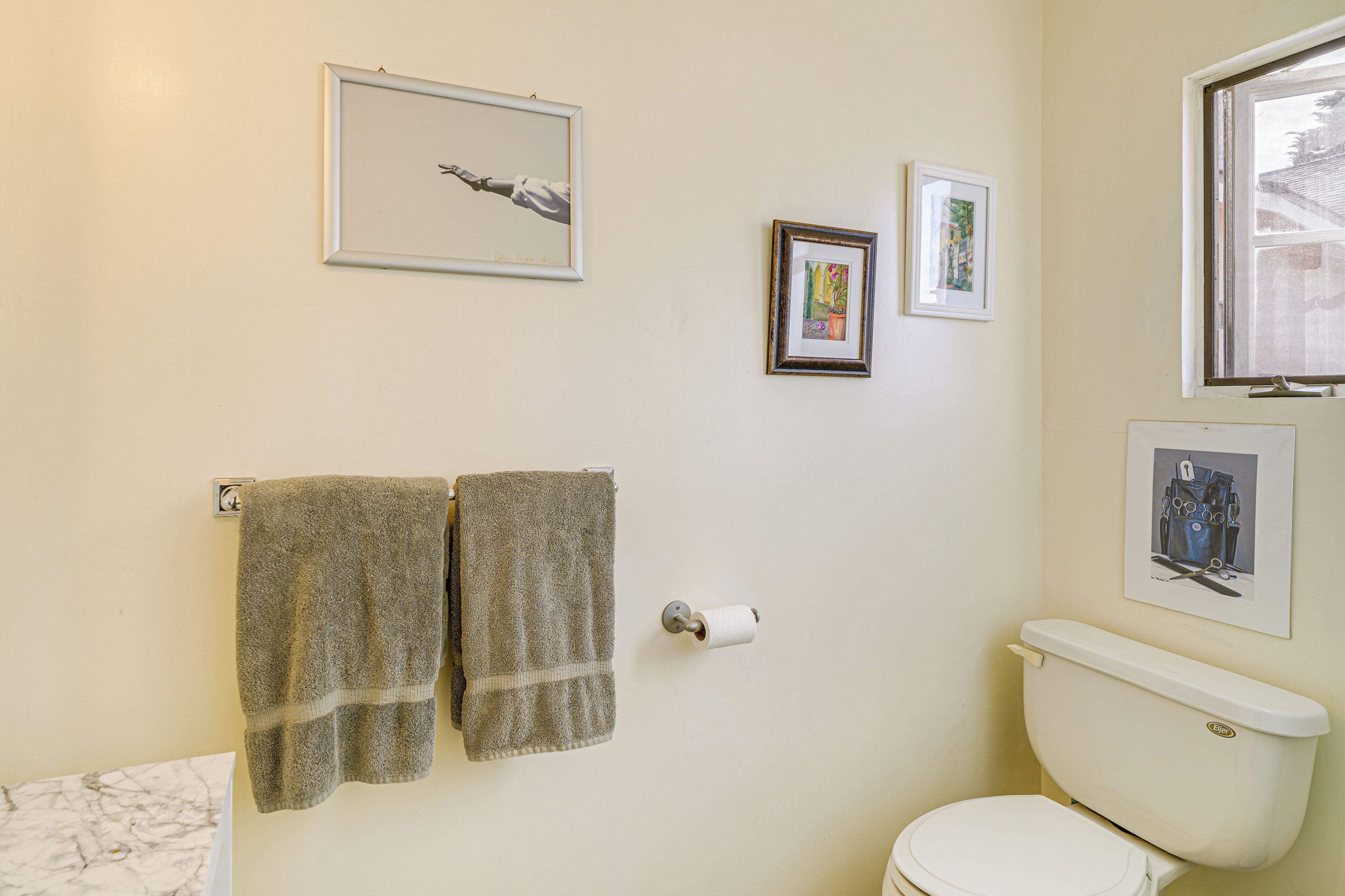 Une salle de bain avec des toilettes, deux serviettes suspendues à un porte-serviettes et trois tableaux encadrés accrochés au mur.