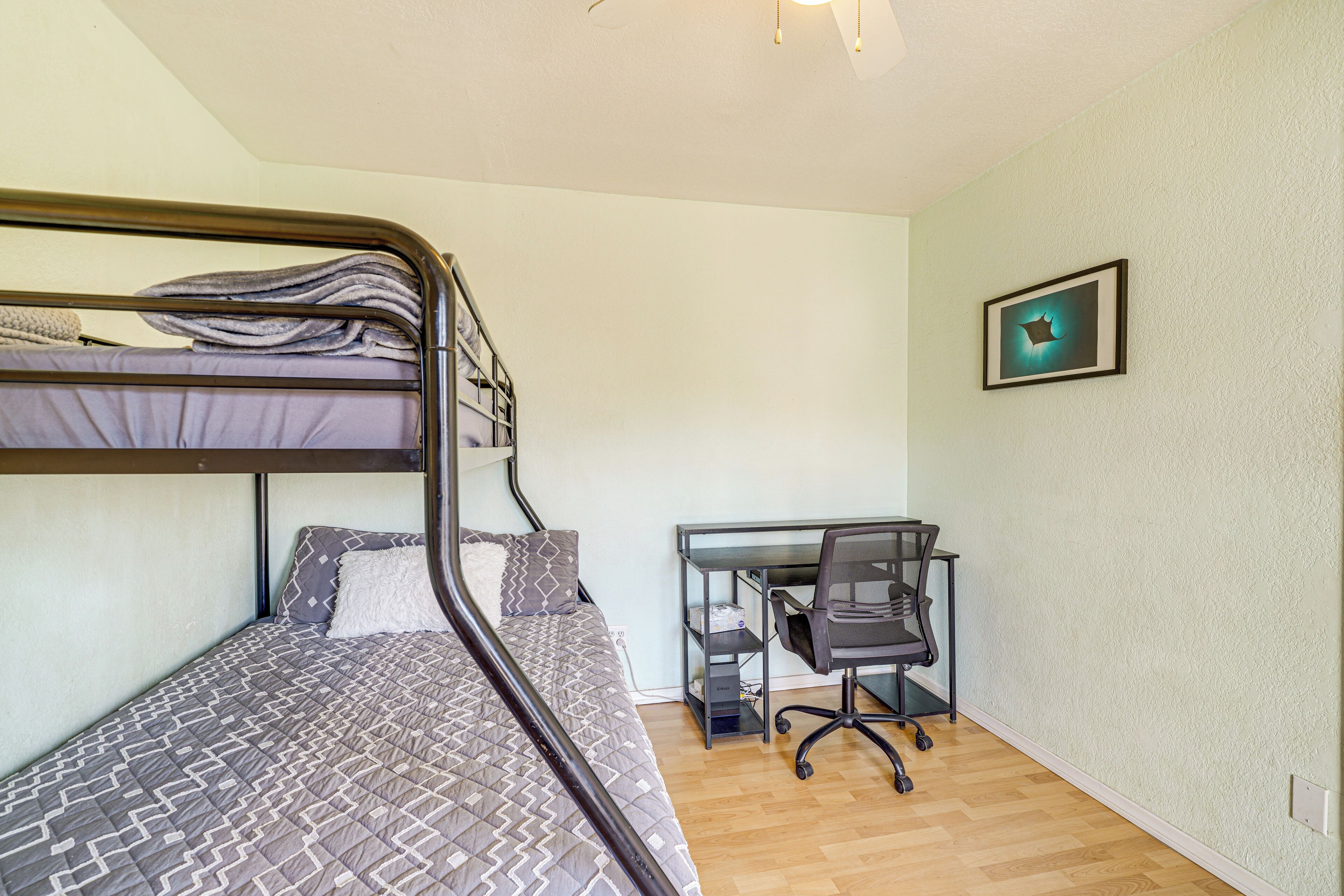 A bunk bed with a desk and chair, a framed picture on the wall, and a light switch.