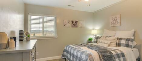 A bedroom with a bed, a ceiling fan, a window with blinds, a dresser, and wall art.