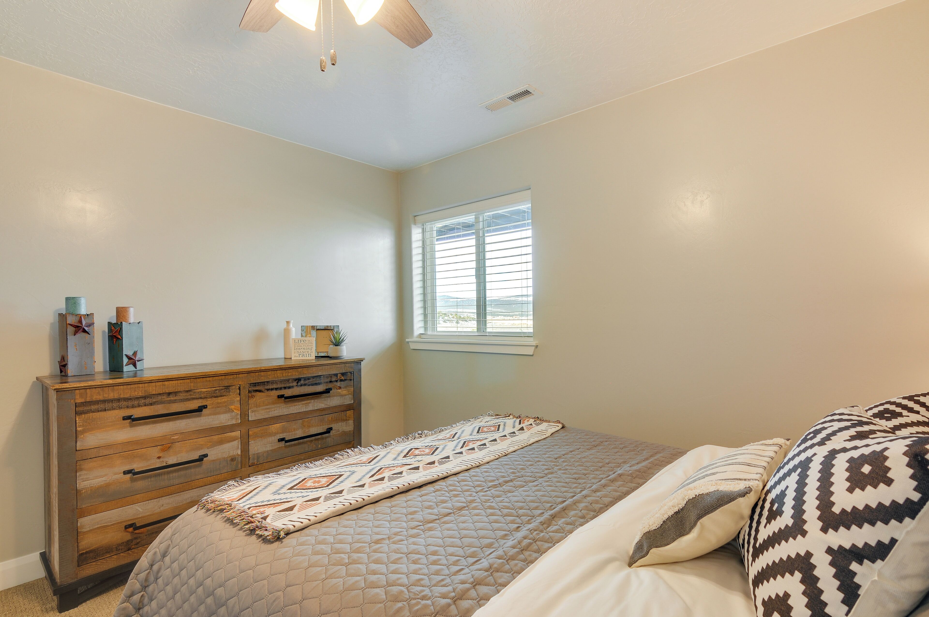 A bedroom with a bed, a dresser, a window, and a ceiling fan.