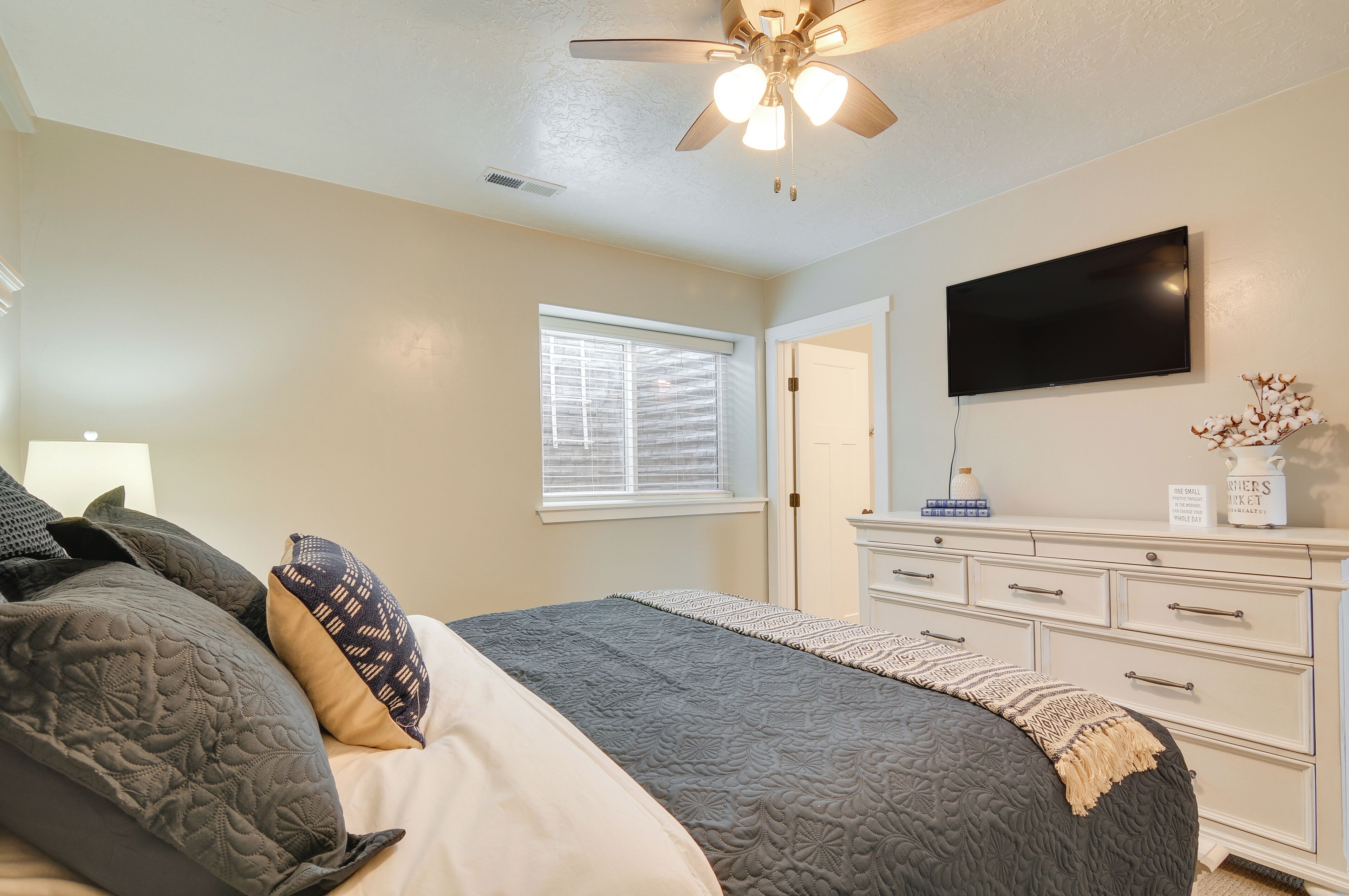 A bedroom with a bed, a ceiling fan, a TV, a dresser, and a window with blinds.