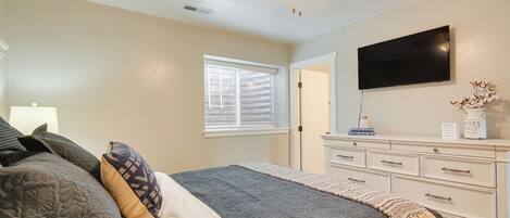 A bedroom with a bed, a ceiling fan, a TV, a dresser, and a window with blinds.