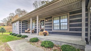 A log cabin-style house with a covered porch, a front door with a wreath, and a small garden area with shrubs and a decorative planter. - Secluded Retreat on 2 Acres Near Dale Hollow Lake! (Burkesville)