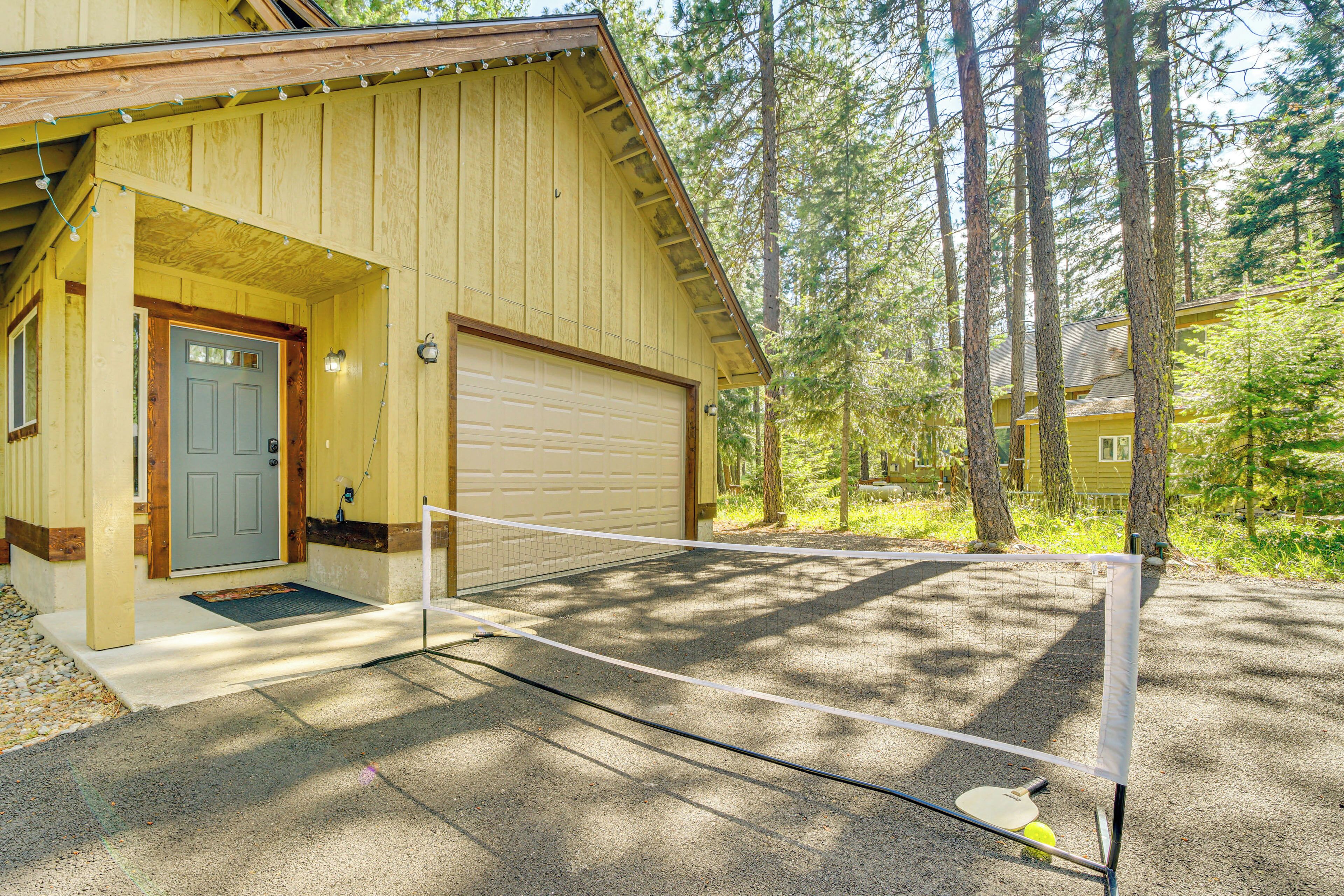 A wooden cabin with a garage, a tennis court, and a forested backdrop.