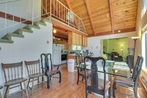 A spacious living area with a wooden staircase, a dining table with chairs, and a kitchen in the background.