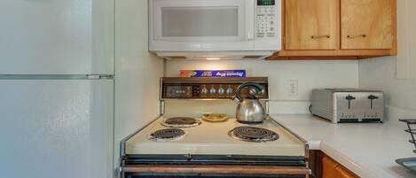 A kitchen with a white refrigerator, a microwave, a stove with four burners, and a toaster.