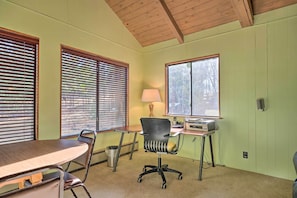 Une pièce avec un plafond en bois, un bureau avec une lampe, une chaise et une fenêtre avec des stores.