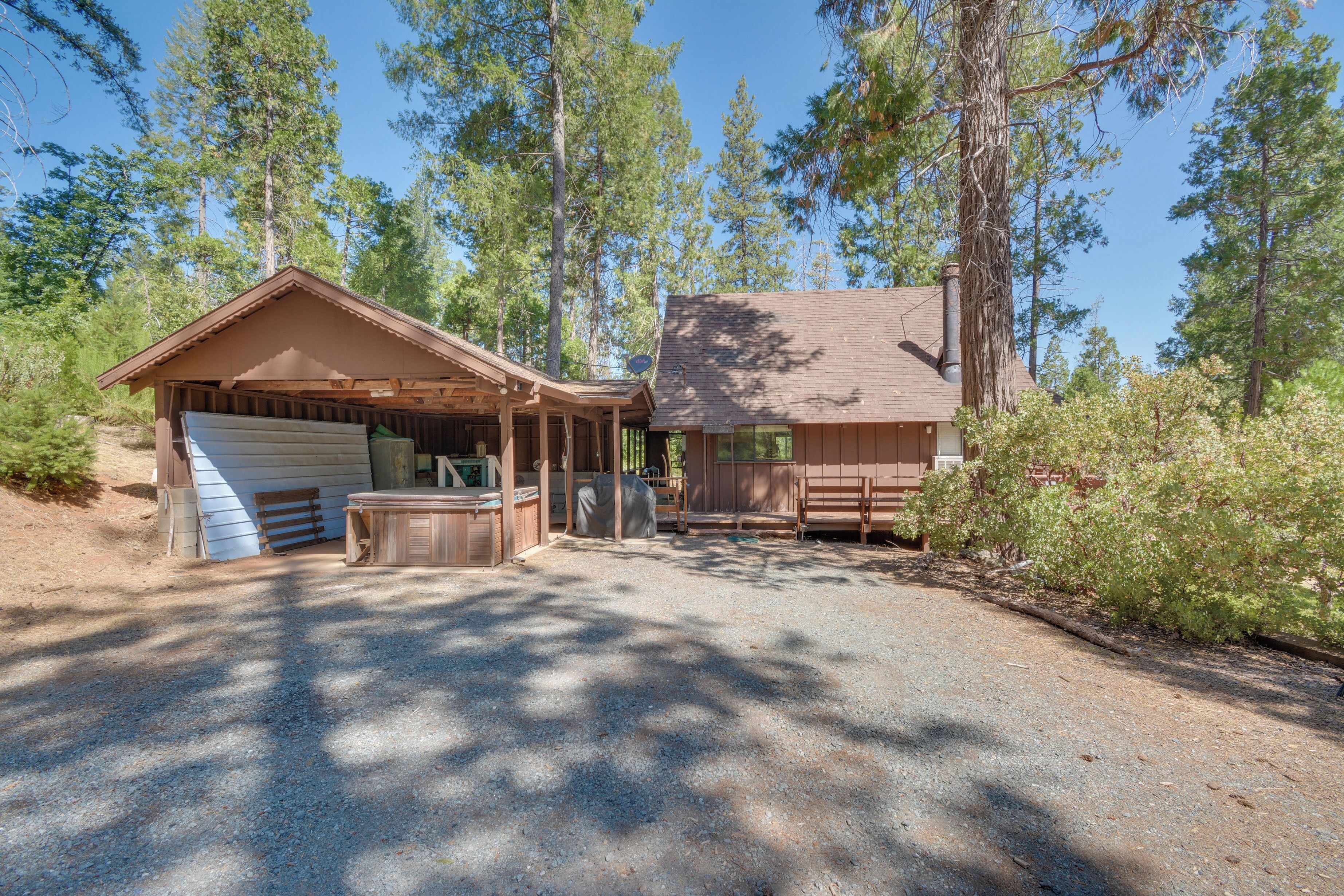 A rustic cabin with a covered porch and a garage, surrounded by tall pine trees.