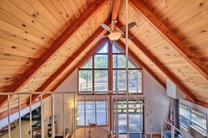 A high-ceilinged room with wooden beams, a ceiling fan, large windows, and a view of the outdoors.