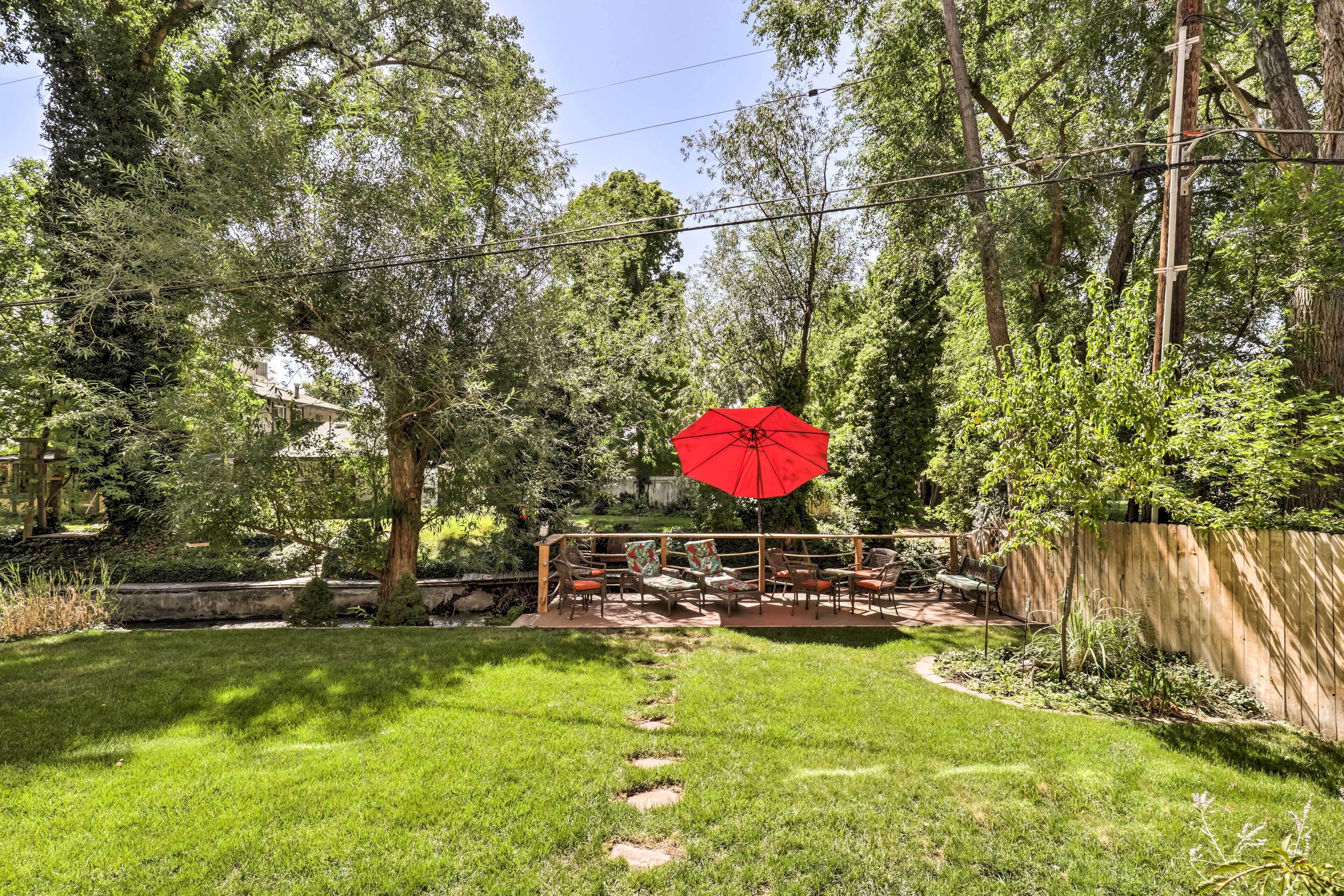 A backyard with a wooden deck, outdoor furniture, and a red umbrella.