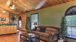 A cozy living room with a wooden ceiling, a sofa with patterned cushions, a coffee table, and a small bear figurine.