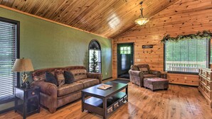 A cozy cabin interior with wooden walls, a green accent wall, a sofa, a coffee table, a chair, and a dresser.