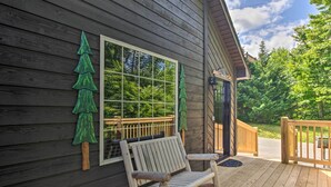A wooden deck with a bench, a window with a view of trees, and a wooden fence.