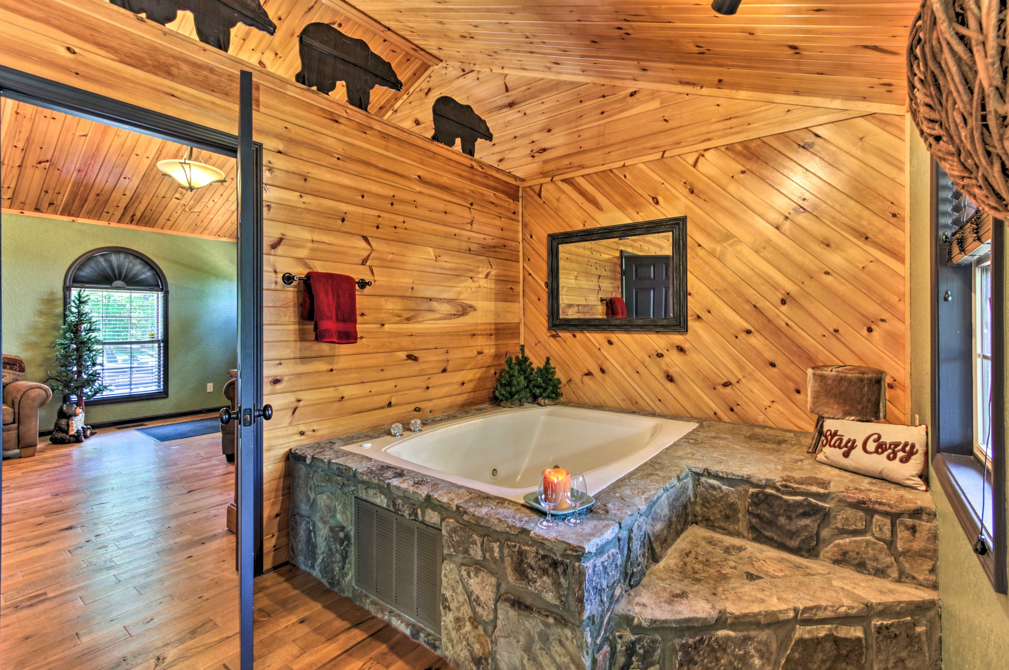 Baño de cabaña de troncos con una bañera de piedra, un espejo y una almohada que dice 'Stay Cozy'.