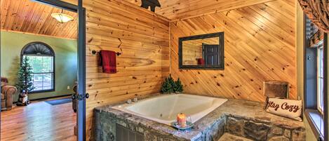 Baño de cabaña de troncos con una bañera de piedra, un espejo y una almohada que dice 'Stay Cozy'.