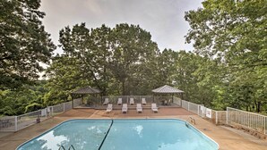 Una piscina rectangular con un trampolín, rodeada por una valla blanca y sillas de deck.