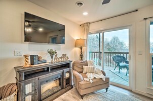 A living room with a fireplace, a television mounted on the wall, a sofa, and a view of the outdoors through a sliding glass door.