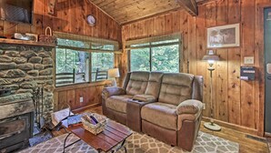 A cozy cabin interior with a stone fireplace, leather sofa, and large windows offering a view of the outdoors. - Secluded Stanardsville Cabin w/ 10 Acres & Hot Tub (Stanardsville)