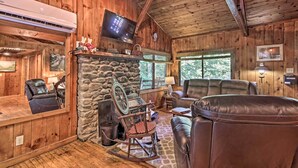 A cozy cabin interior with a stone fireplace, leather furniture, and a television mounted on the wall. - Secluded Stanardsville Cabin w/ 10 Acres & Hot Tub (Stanardsville)
