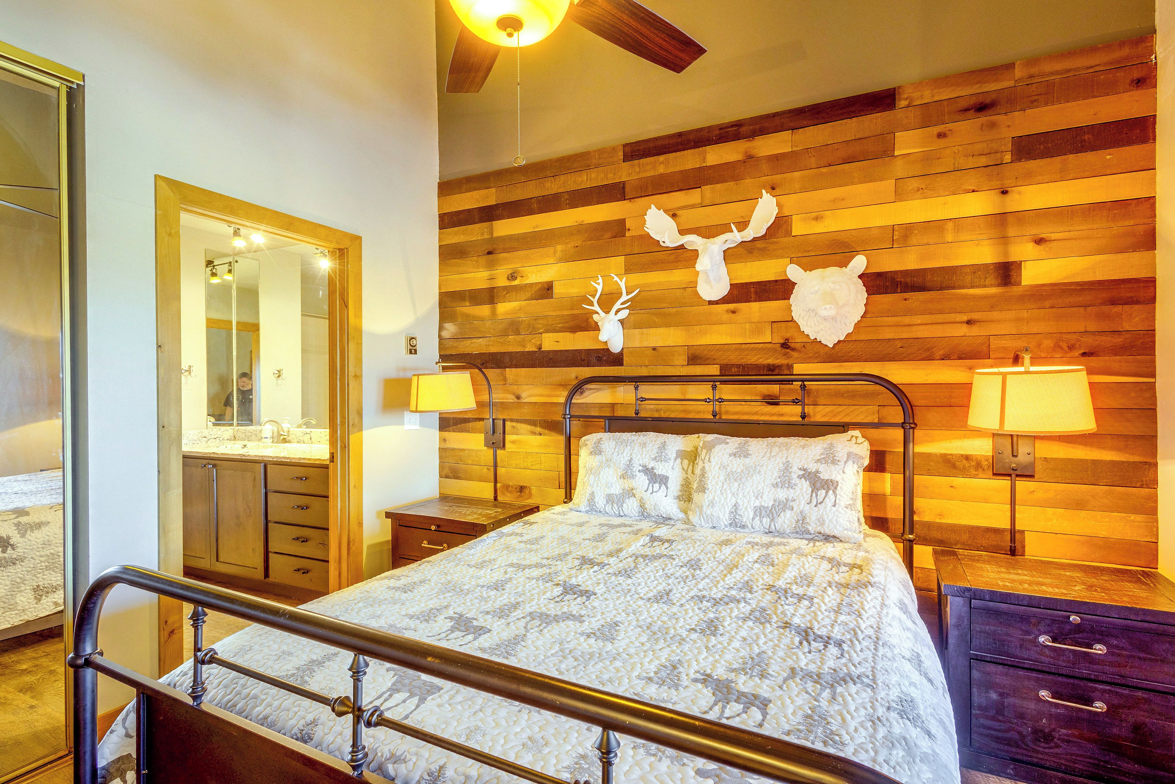 Quarto com cama, cabeceira de madeira, espelho e mesa de cabeceira com abajur.