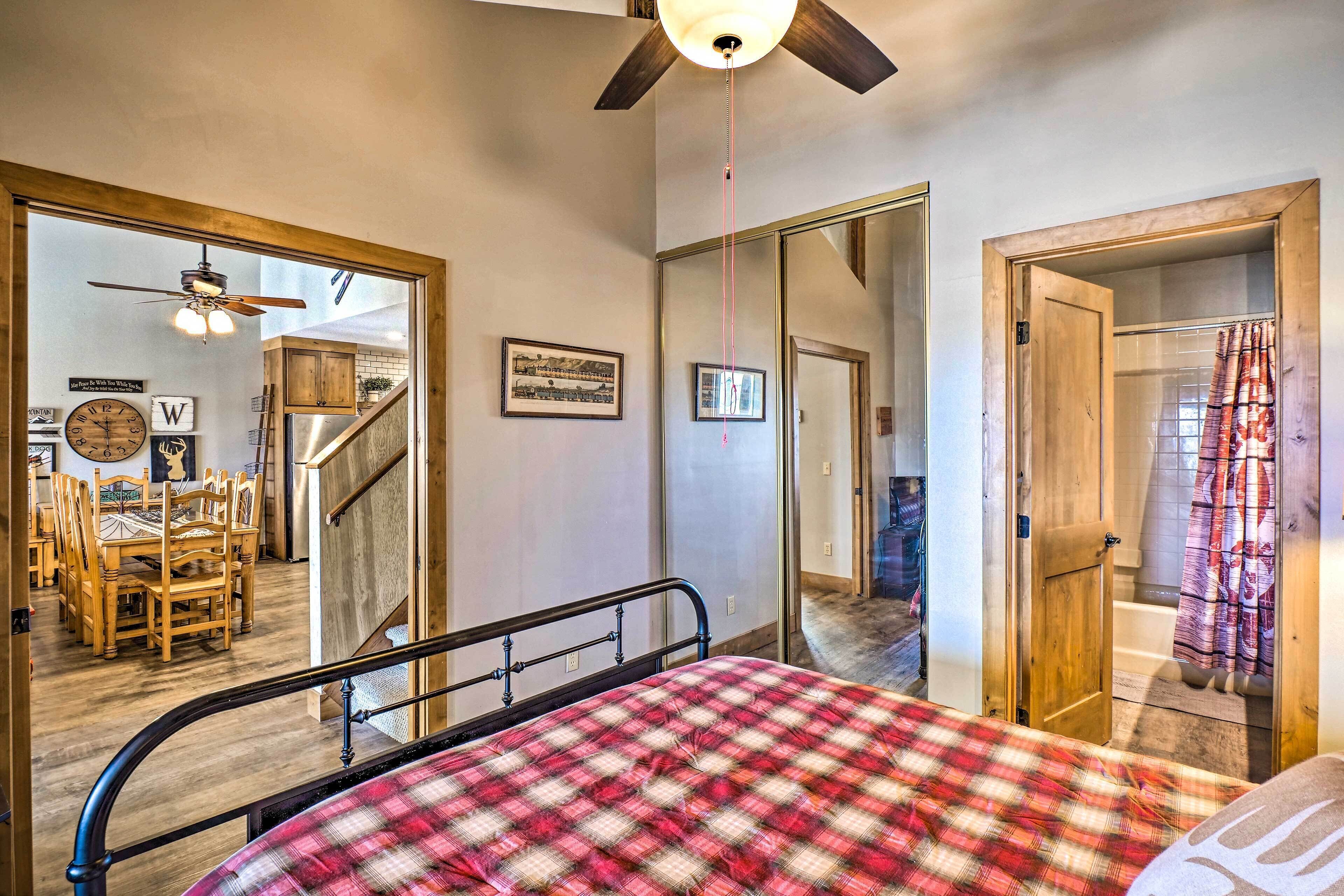 A bedroom with a bed, a ceiling fan, a wooden door leading to a bathroom, and a dining area with a table and chairs.