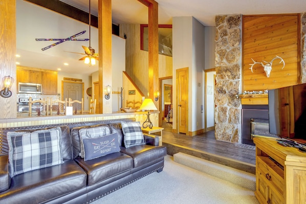 A modern living room with a leather sofa, a stone fireplace, and a kitchen in the background.