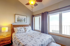 A bedroom with a bed, a nightstand, a lamp, a ceiling fan, a window with curtains, and a framed picture on the wall.
