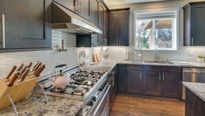 A modern kitchen with dark wood cabinets, a stainless steel stove, and a large window providing natural light. - Spacious Carnation Home w/ Grill & Large Yard (Carnation)