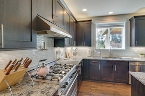 A modern kitchen with dark wood cabinets, a stainless steel stove, and a large window providing natural light. - Spacious Carnation Home w/ Grill & Large Yard (Carnation)